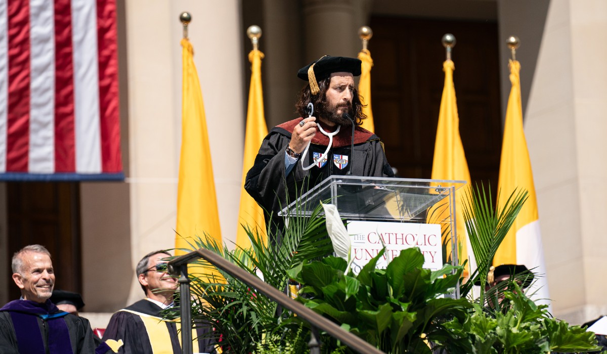 Jonathan Roumie, after receiving an honorary doctorate, lifts up a stethoscope during his address to graduates on Saturday. 