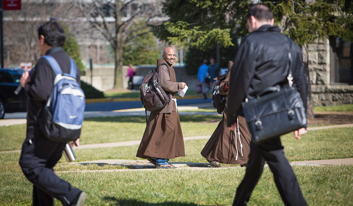 friars walking across campus wearing backpacks and their brown habits