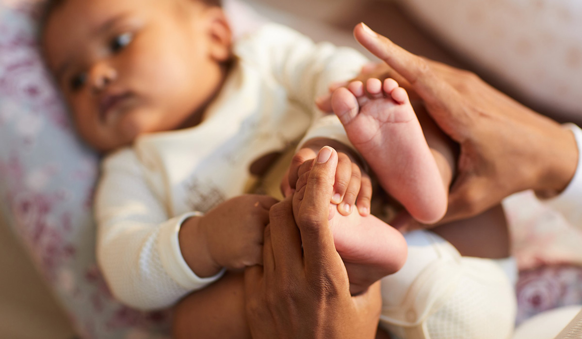 mom's hands playing with baby laying on its back