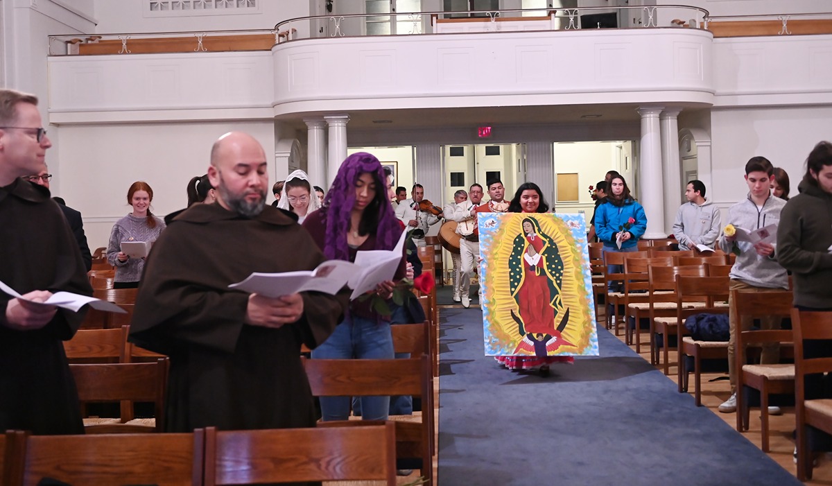 A student rolls a portrait of our lady of guadalupe down an aisle