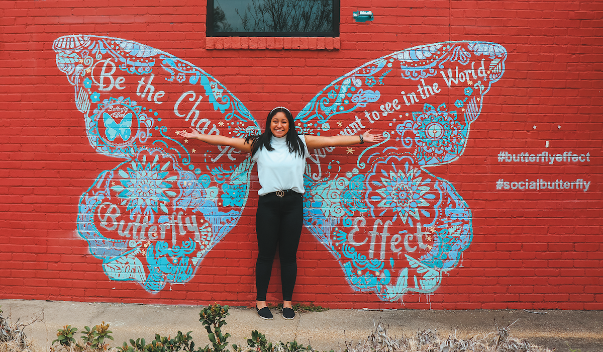 Student Darby Drake poses in front of a mural inspiring change in the world.