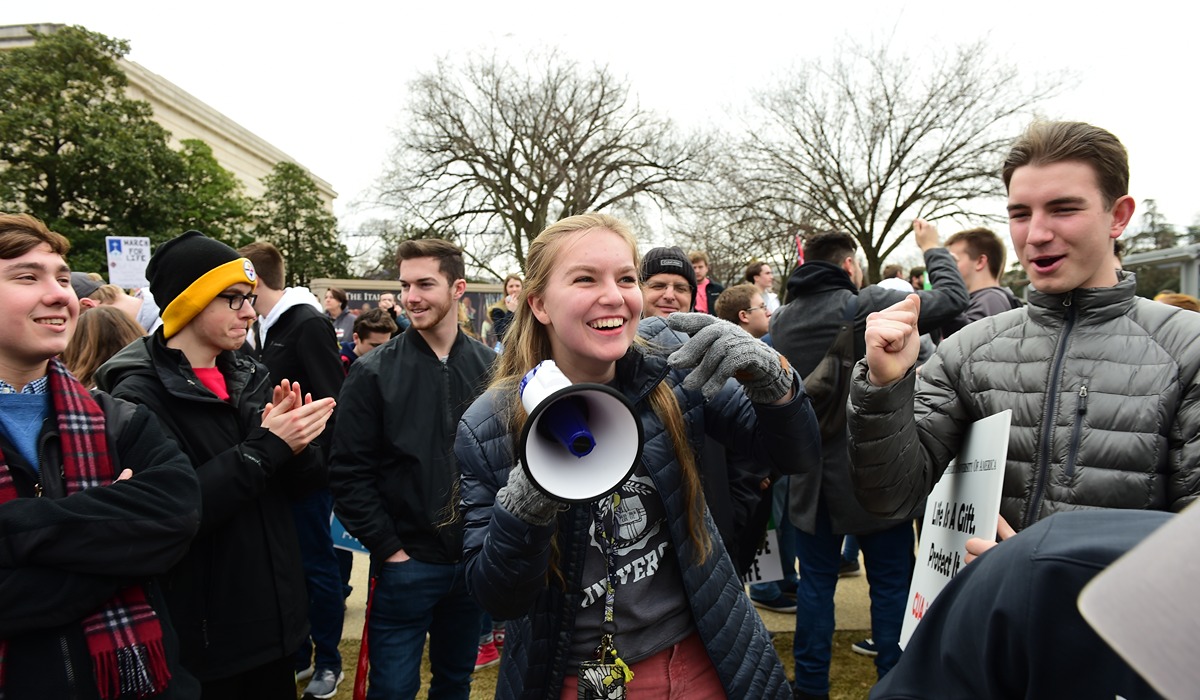 A student holds a bullhorn surrounded by other students smiling