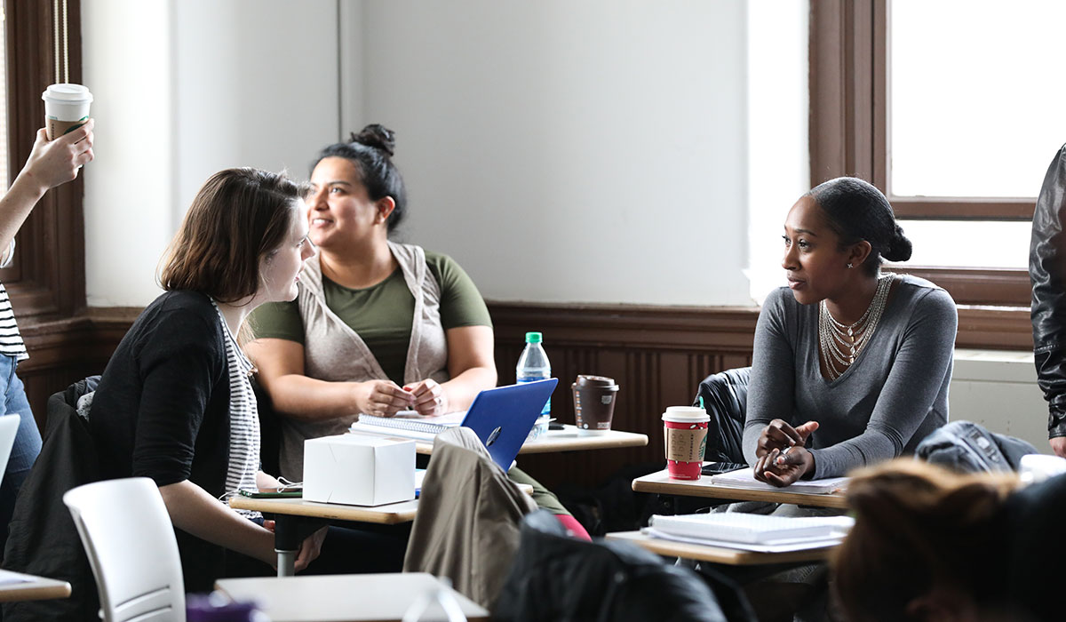 A group of students sit around desks, discussing a project.