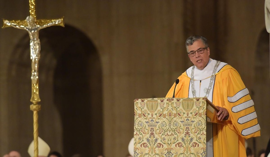 President Kilpatrick speaking at a podium in the basilica in a yellow robe