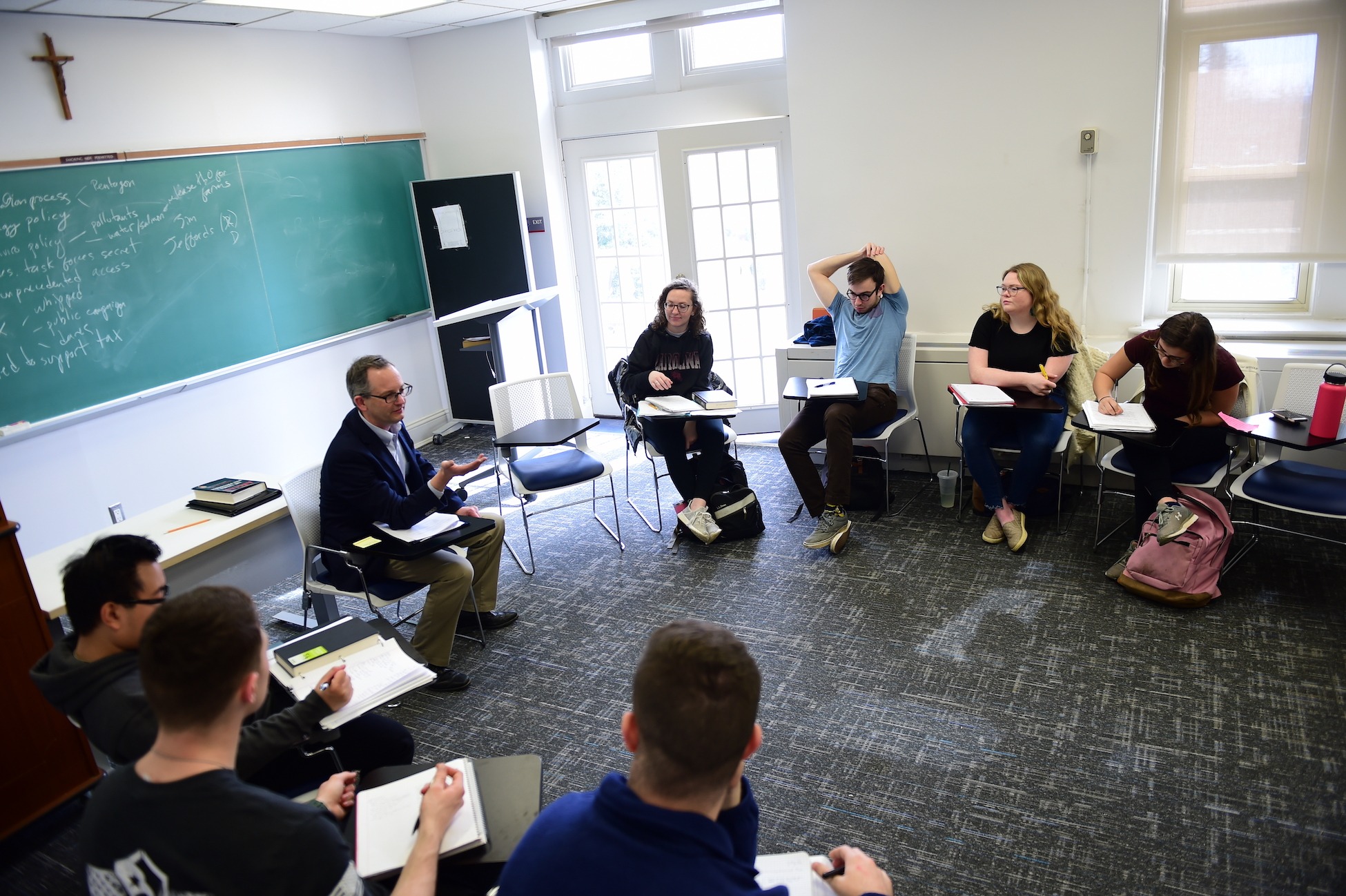 professor and students sit with their desks in a circle for a class discussion