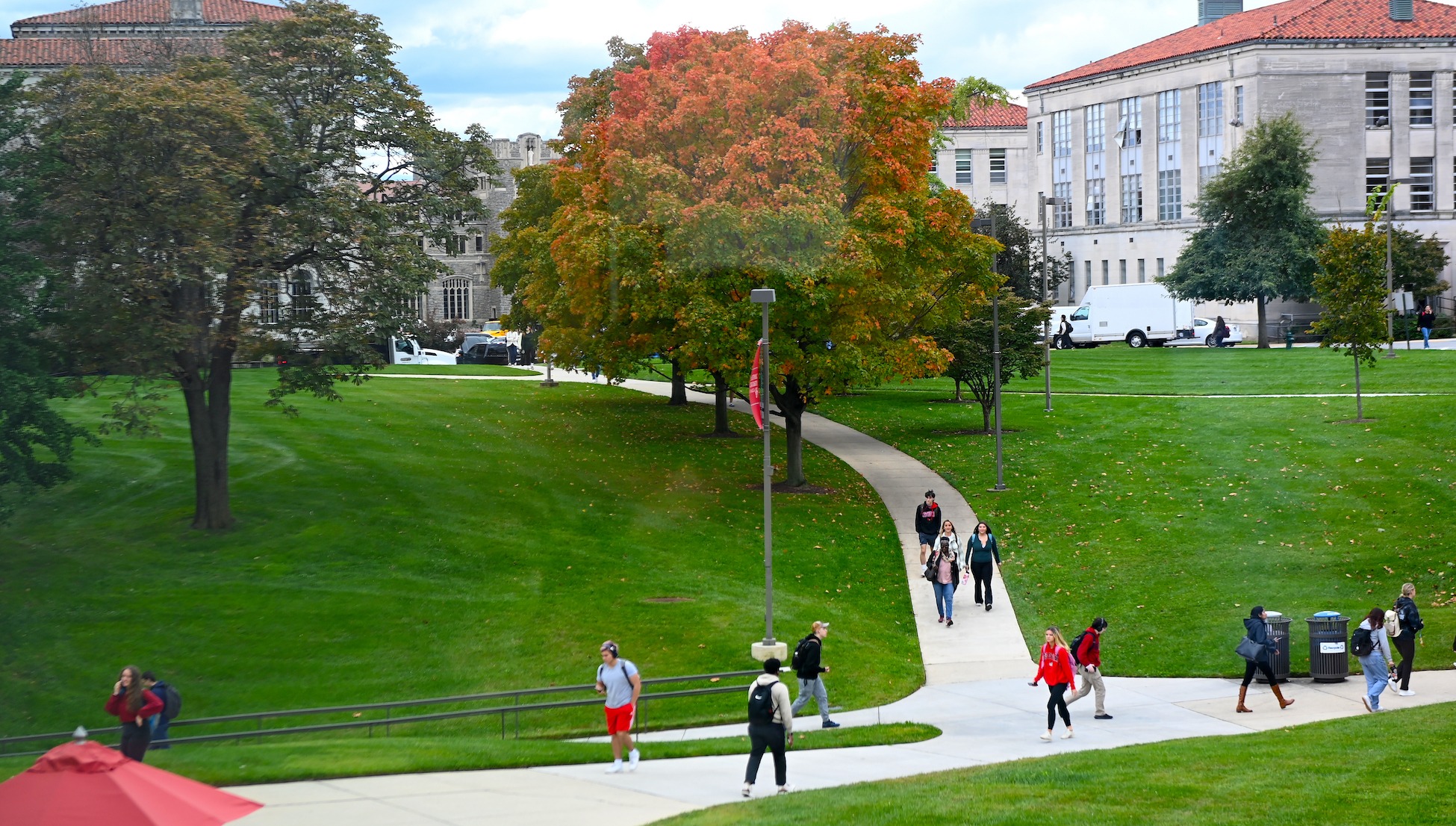 students walking across campus with orange fall trees in the background