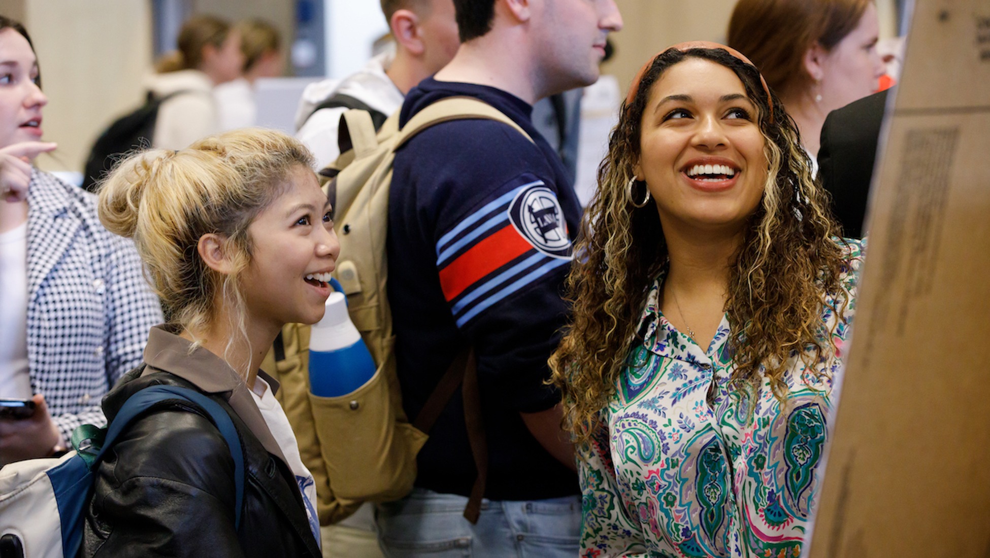 students smiling as they look at a poster presentation at university research day