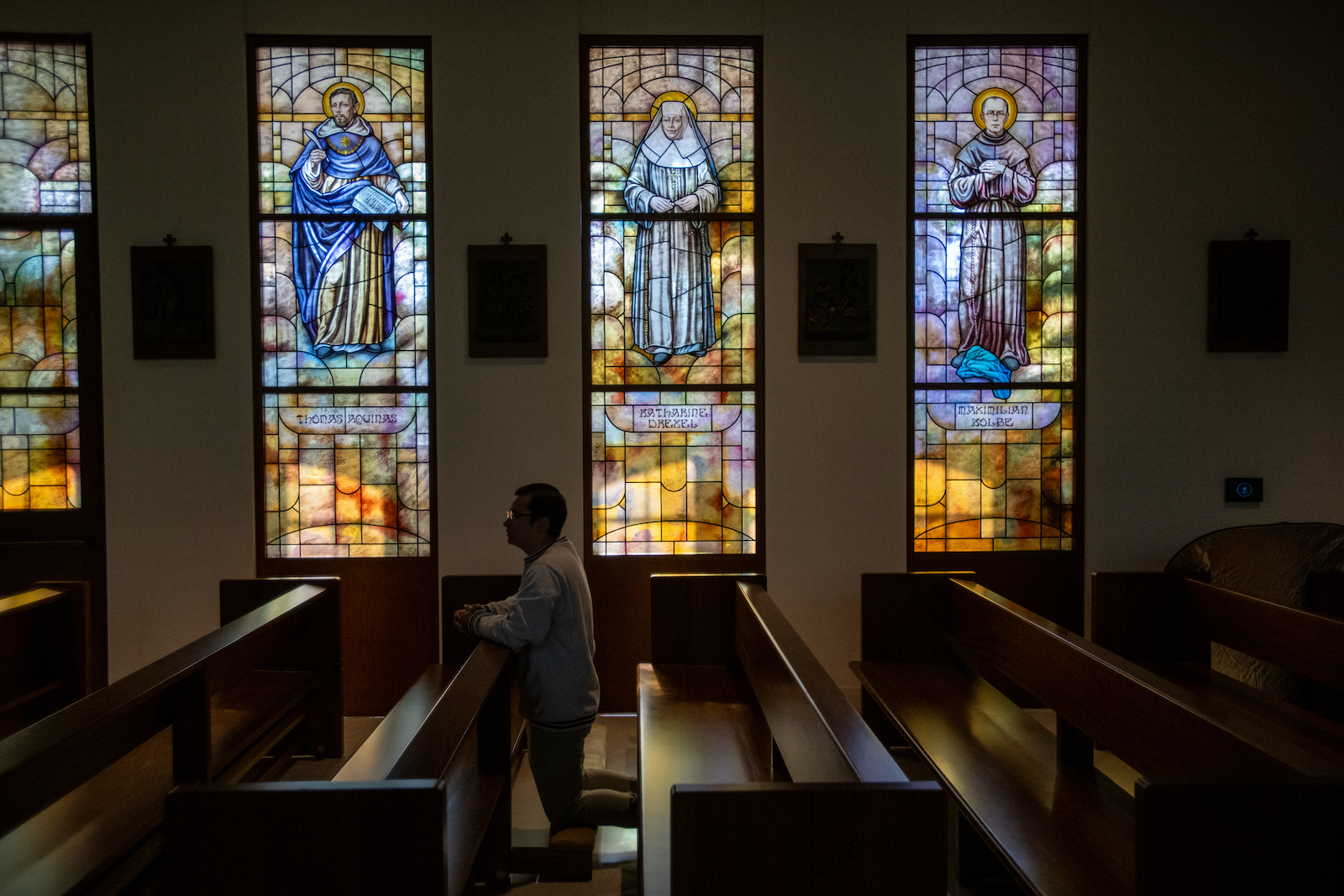 student praying amidst a backdrop of stained glass windows in a chapel on campus