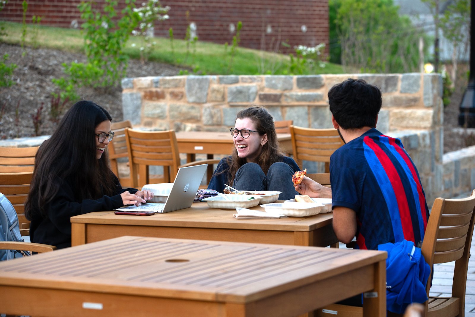 students smiling and talking at a picnic table outdoors on campus