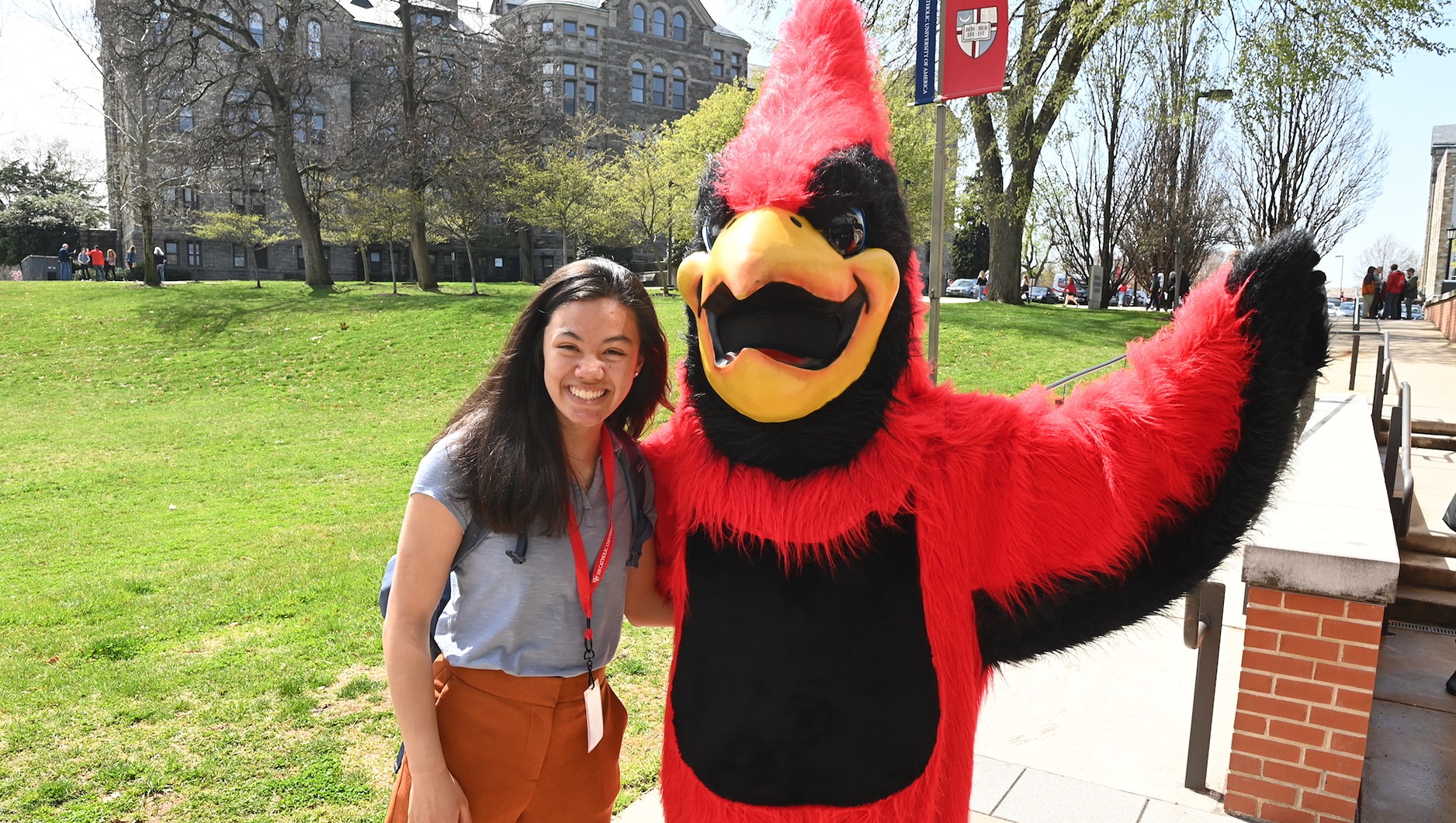 student takes a picture with Red the cardinal, the catholic university mascot