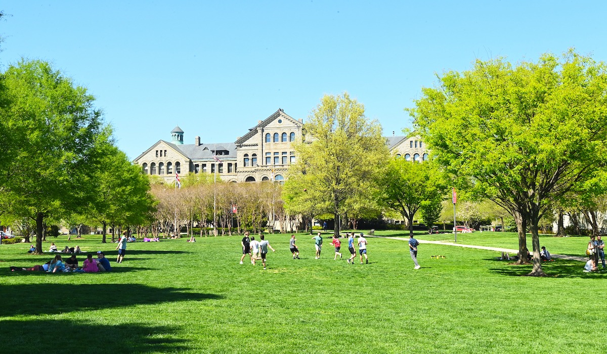 green campus lawn with students playing in the distance