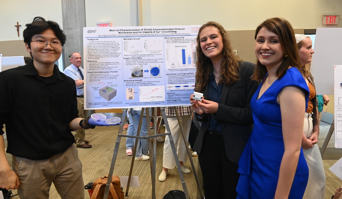 Maria Erquiaga stands in front of her poster at University Research Day with two other students.