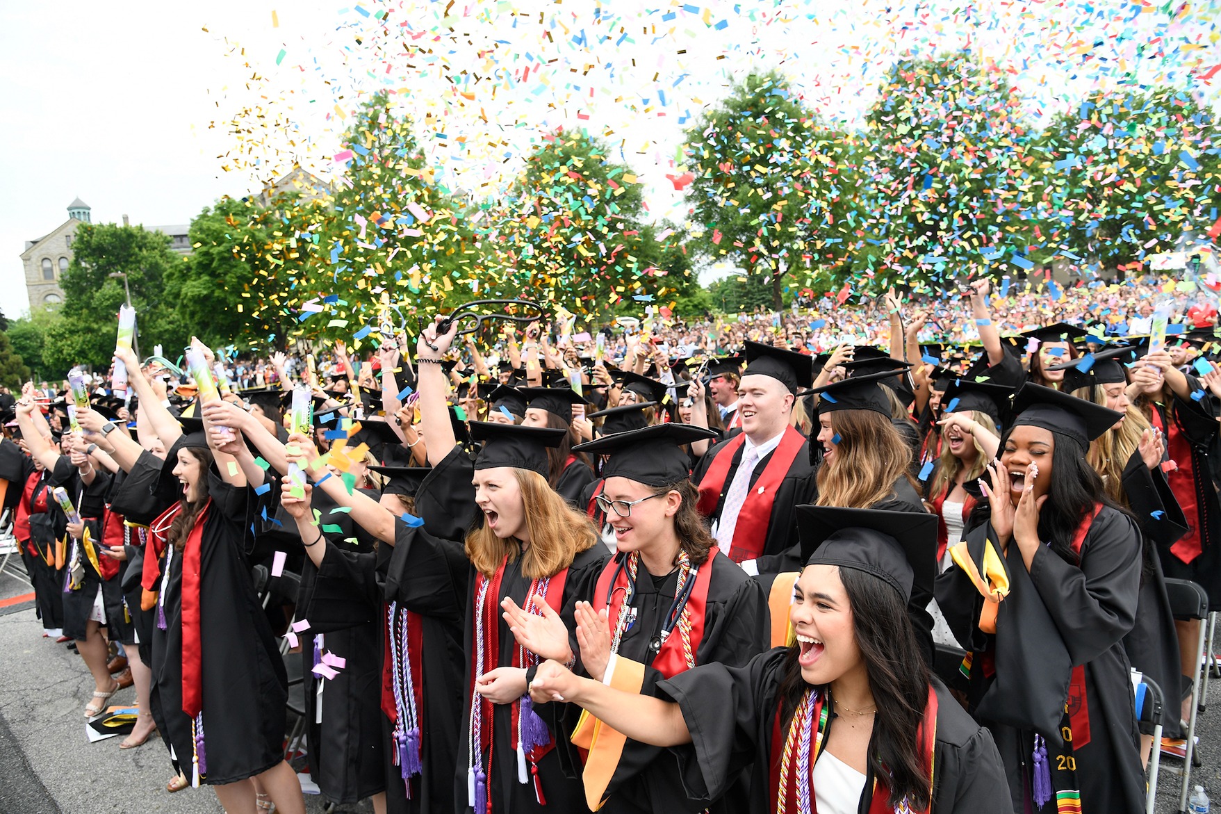 graduates cheer and throw confetti in the air at their graduation ceremony