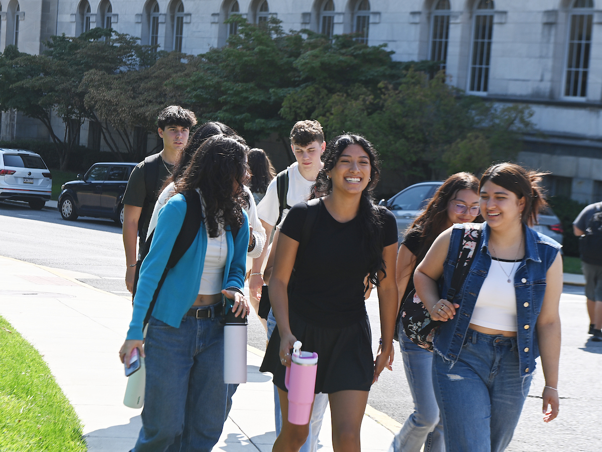 A diverse group of students gather on the sidewalk on the way to class.