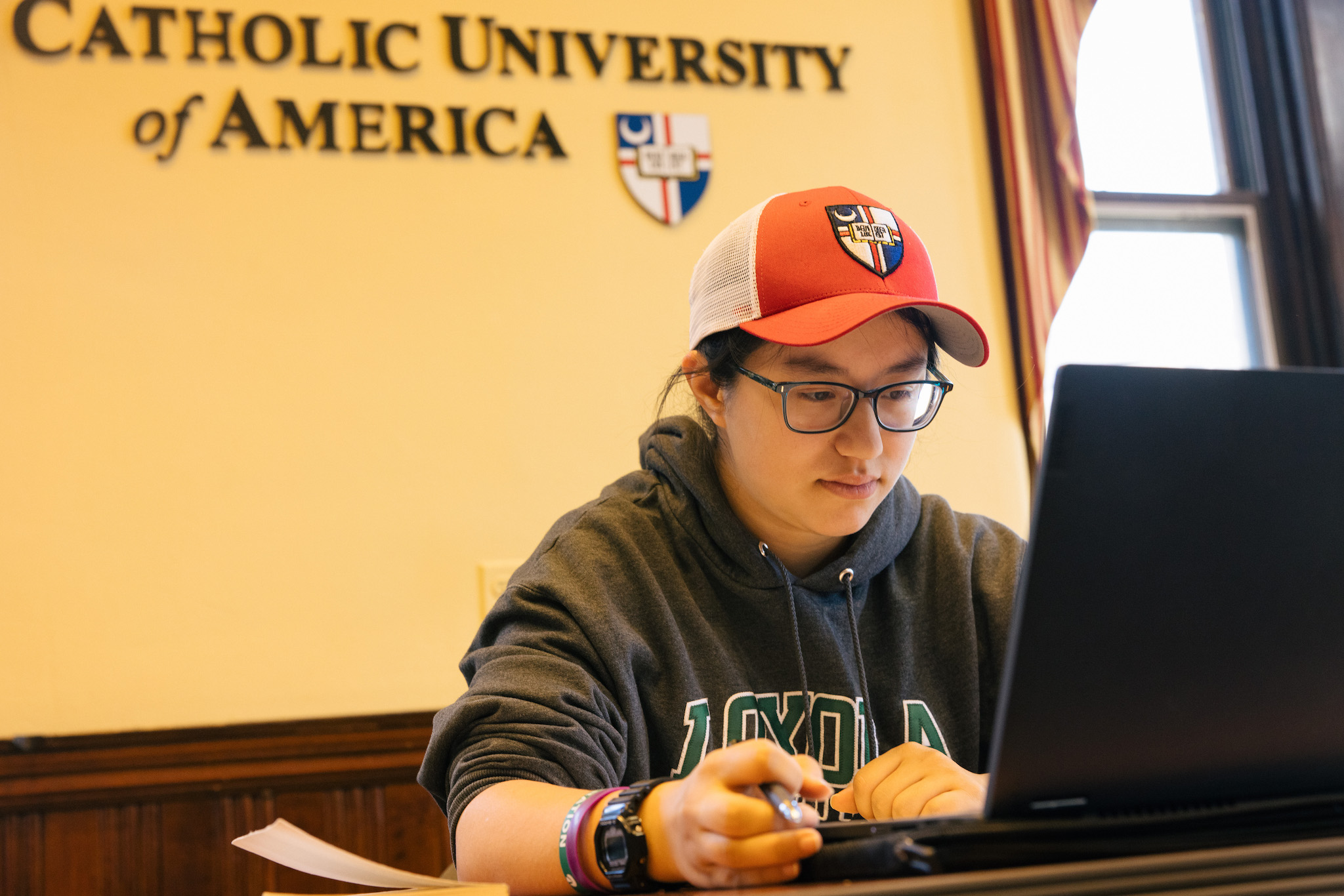 student in a CUA hat looking at a computer working