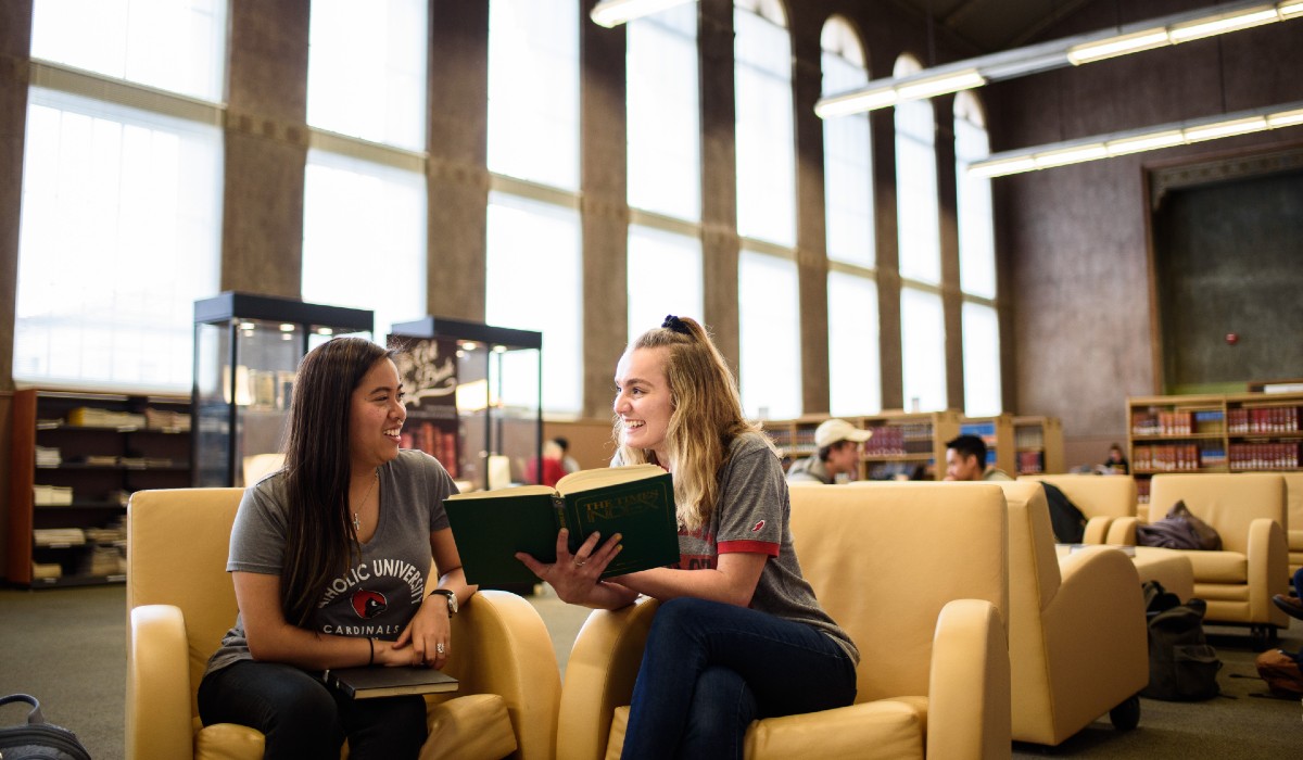 Two students sit together in Mullen Library, reading a book.