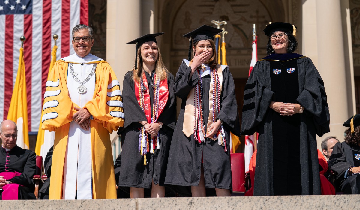 Maria Erquiaga stands in her graduation robe with one other graduate and two University members, including President Kilpatrick.