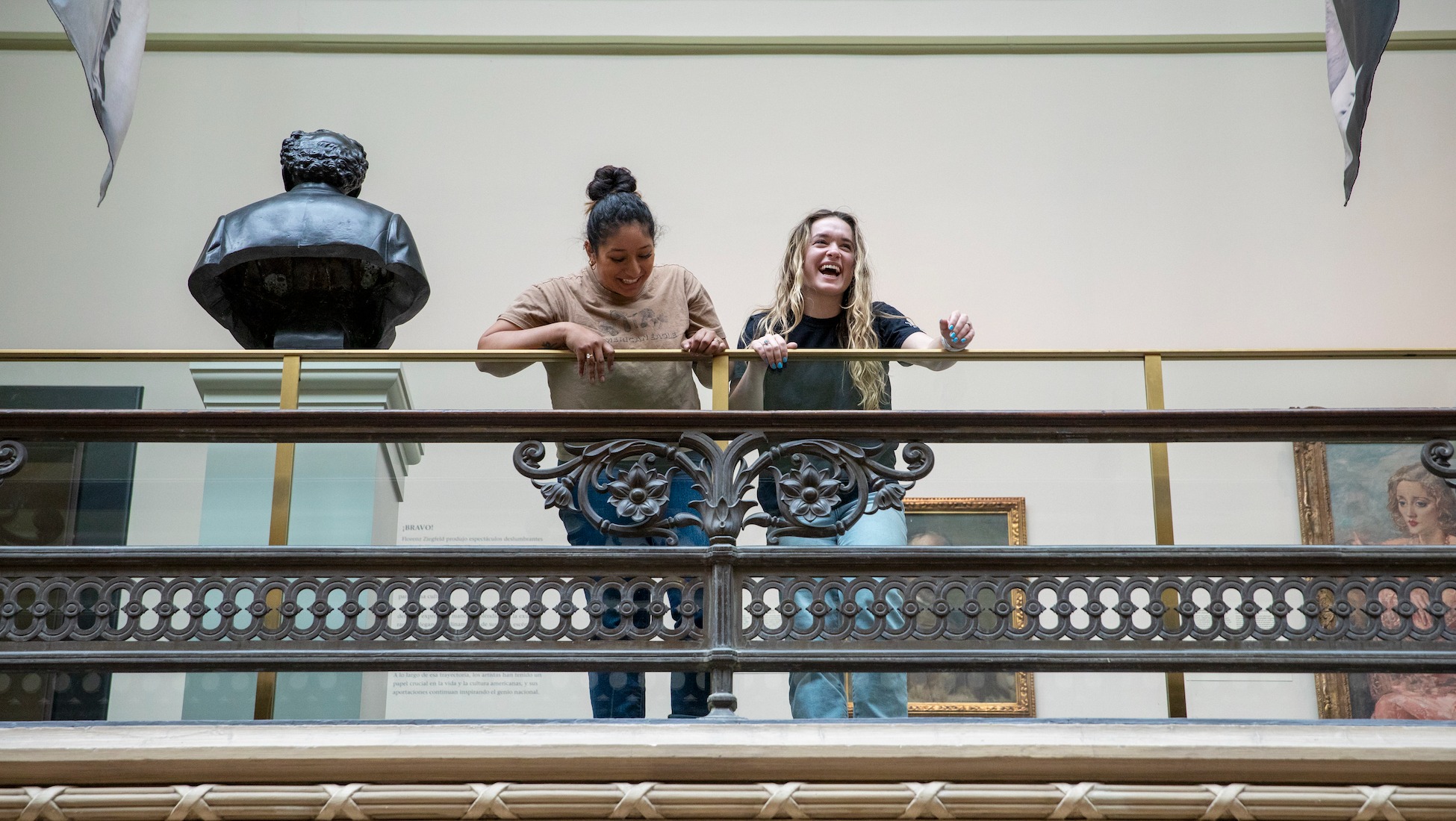 students standing on a balcony in a museum and laughing