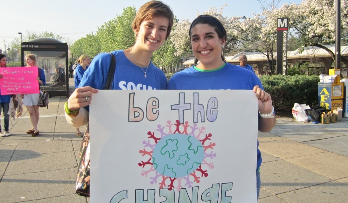 two students holding a self created sign that says be the change