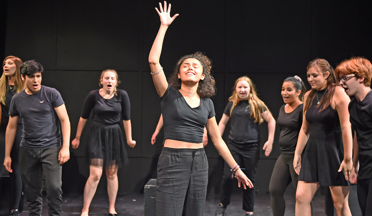 students performing a drama on stage in all black