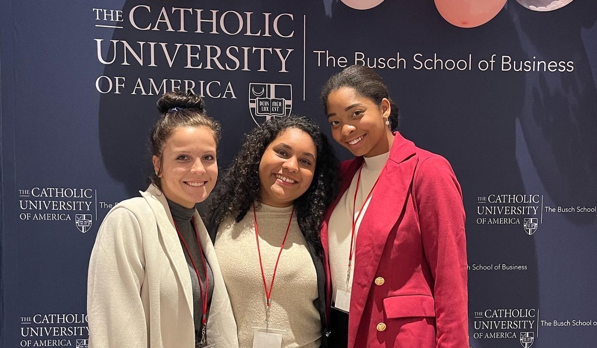 Lauren White stands with two other Catholic University students. She is wearing a bright pink suit.