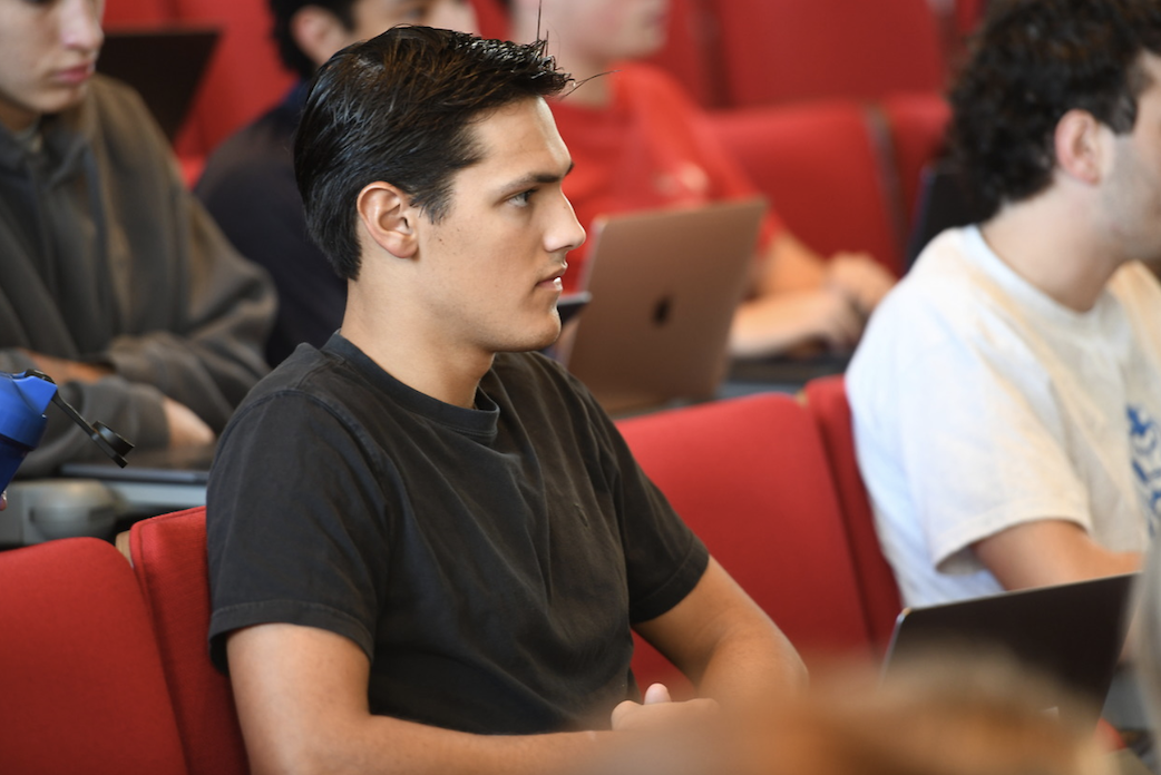 male student in a black tee sitting in a lecture hall