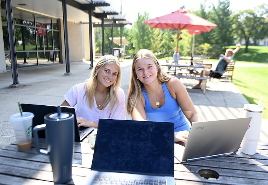 two female students outside on their laptops at a table