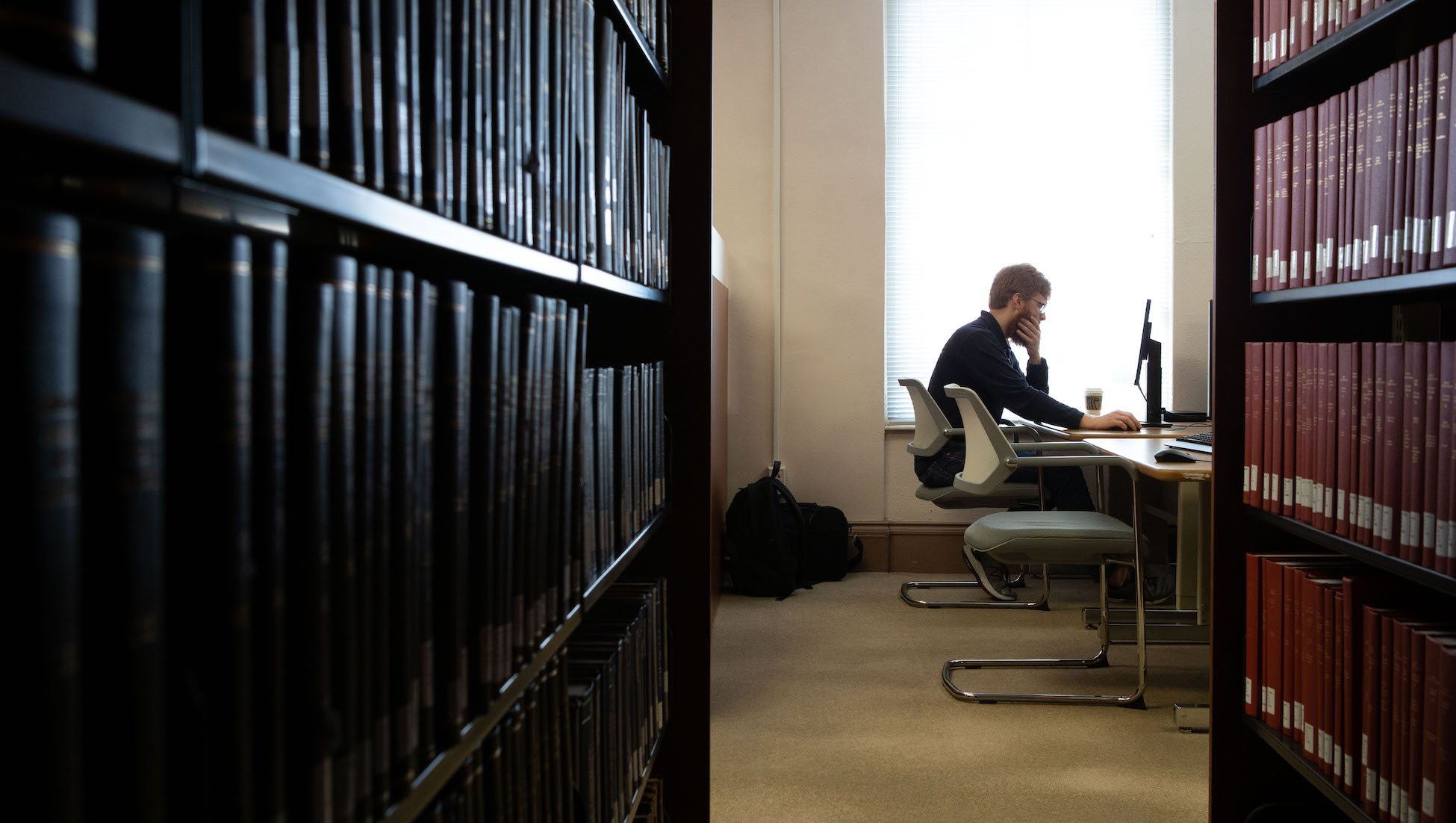 student doing schoolwork in the library behind shelves of books