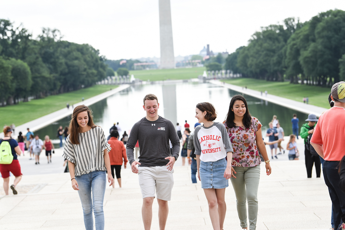 Four students are walking up the Lincoln Memorial steps, with the Washington Monument and the reflecting pool behind him.