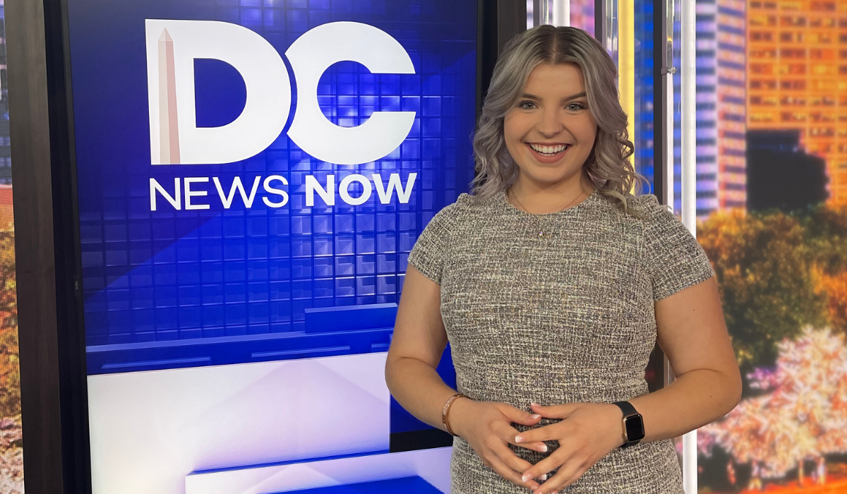 Alexis is at her internship with DC News Now, standing infront of the blue digital sign.