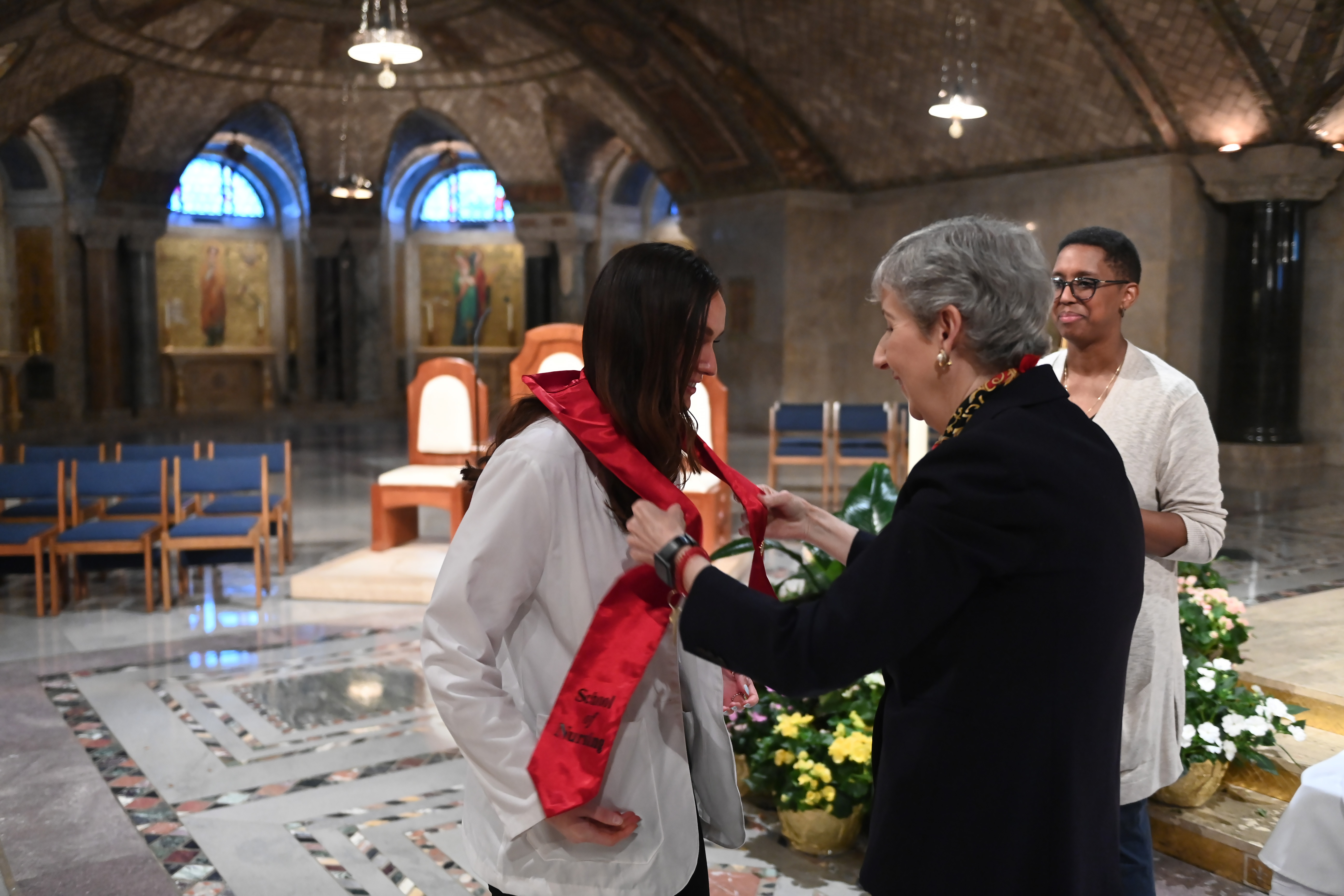 Marie Nolan, dean of the Conway School of Nursing, attaches the nursing pin to a graduate’s stole