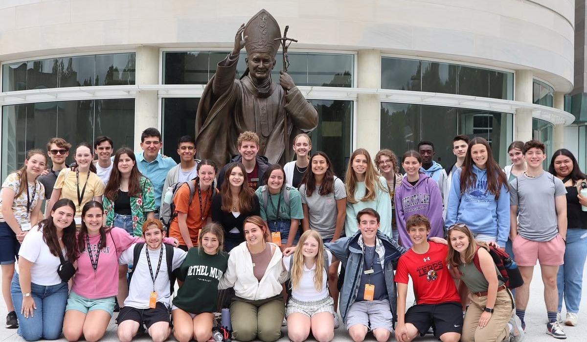 Students posing in front of a statue of the pope