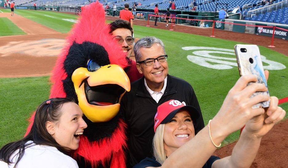 President kilpatrick posing for a selfie on the nationals baseball field with the cardinal mascot and others