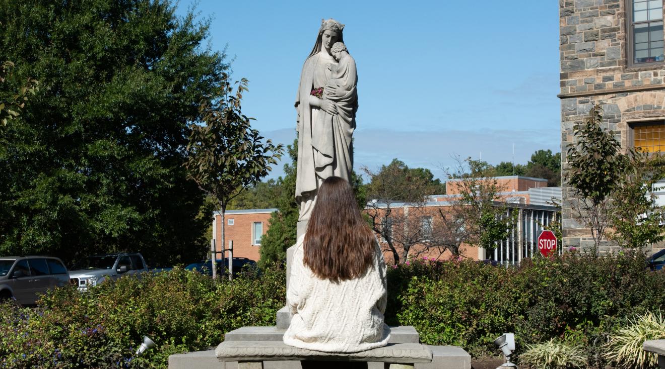 student praying at a mary statue on campus