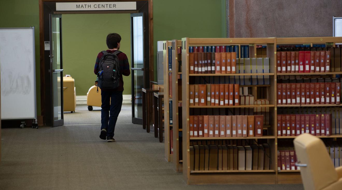 student walking in the library next to a shelf of books